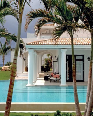 Palm trees offer shade and privacy to an infinity pool that wraps around the corner of a villa veranda supported by pillars