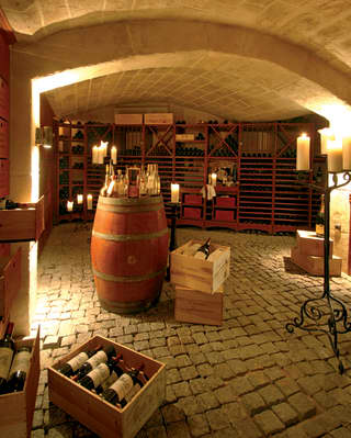 Pillar candles offer extra charm to this cobbled-floor, vaulted-ceiling wine cellar, with shelves of bottles and authentic barrel