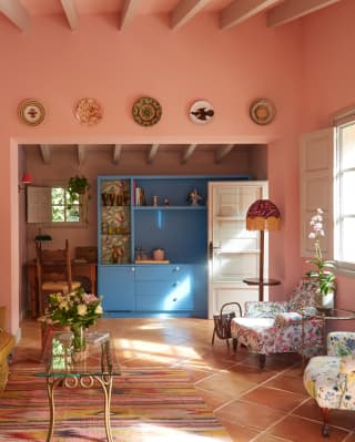 Rustic and vibrant, the lounge delights with pink walls, bronze sofa, floral armchairs, blue cabinets and eclectic prints.