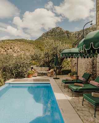 View of the length of the villa pool, with a row of green loungers and parasols to the right, and rocky, hillside views.