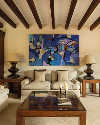 An enormous blue abstract painting hangs above the cream sofa of a chic sitting room, flanked by large table lamps