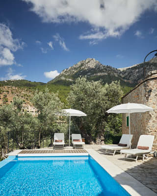 A limestone crag descending into olive groves dominates the skyline. In the foreground a private pool sparkles in the sunlight