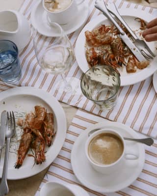 Looking down on a satisfied dining table, where fresh coffees sit by finished plates of prawns and glasses of water and wine.