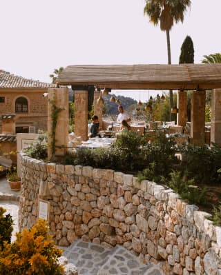 A waiter chats to guests on the terrace of Tramuntana Grill, seen from steps that wind in front of the supporting stone wall.