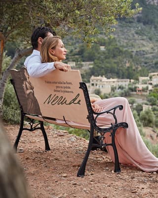 A couple enjoys a view across the hillsides of Deia. On the back of the bench they're sitting on is quote from poet, Neruda