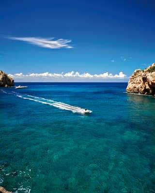 Motor boat speeding along a coastline over clear blue waters on the Mallorcan coast