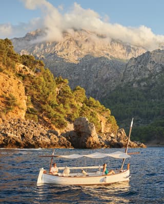 A small wooden sailing boat bobbing on coastal waters with mountains beyond
