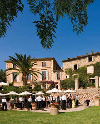 Guests at a garden party among lush gardens outside a stone-built Spanish villa