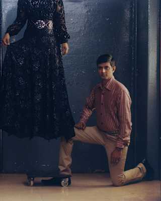 A man in red-striped shirt and beige trousers kneels by a woman in a black lace dress, apparently floating above the floor.