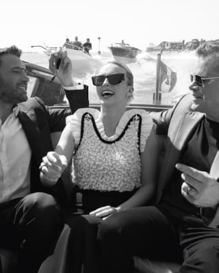 Black and white image of actors Ben Affleck, Jodie Comer and Matt Damon, dressed up and laughing together in a water taxi.