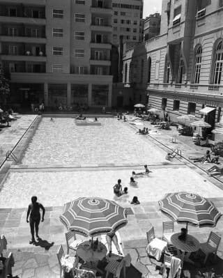 Timeless monochrome shot of the pool, with three parasols and tables, and people lunching and lounging at the poolside.