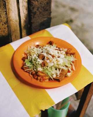 An orange plate of Enchiladas del Portal, comprising a tortilla with beans and vibrant fresh ingredients, seen from above.
