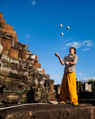 Amid the ruins of a Cambodian temple, a juggler carefully watches three balls in the air