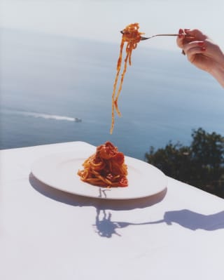 Image from the Liguria cookbook shows a bowl of three-tomato Spaghetti alla Elizabeth Taylor enjoyed at an ocean-view table.