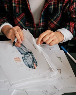 Close-up of two hands holding a pen and flicking through handrawn garment images