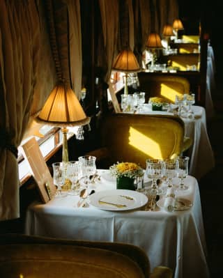 Gold light brushes the green velvet Etoile du Nord dining chairs, in a high-angle view over a laid tables with glowing lamps.