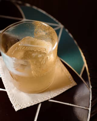 Close-up of Bambuco-branded ice cubes in a half-drunk cocktail in a tumbler set on a coaster on a tiled table top.