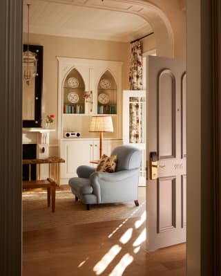 View into Honeysuckle's lounge, where sunshine brushes past a deep-seat blue armchair with a floral cushion by a floor lamp.