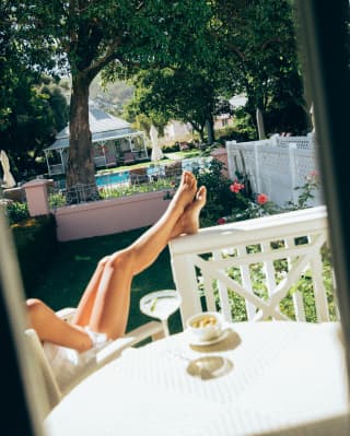 Angled image of a guest on the Honeysuckle Cottage porch, sitting at a table with a cocktail and her legs up on the railings.