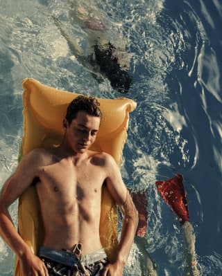 Hombre flotando en un colchón inflable naranja en una piscina