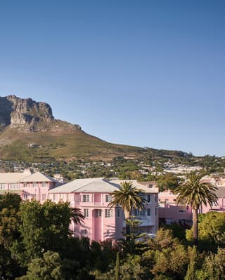 Aerial view of a pink hotel among lush foliage and Table Mountain beyond