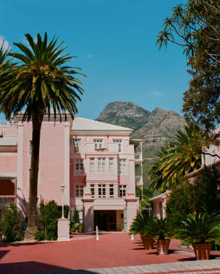 Rugged peaks of the Table Mountain Reserve loom in dusty greens behind the confectionary-pink hotel and deep coral driveway.