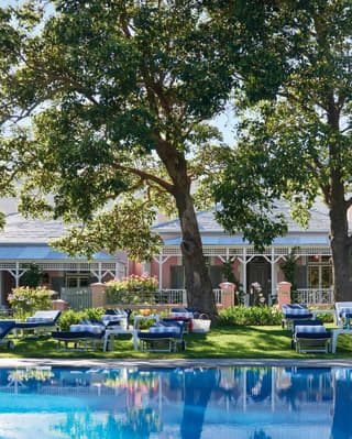 Outdoor hotel pool lined with blue sunbeds reflecting trees and a pink hotel