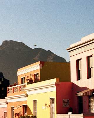 Mountains loom behind bright buildings of orange, pink, yellow and brown, in Cape Town's multicultural Bo-Kaap area.
