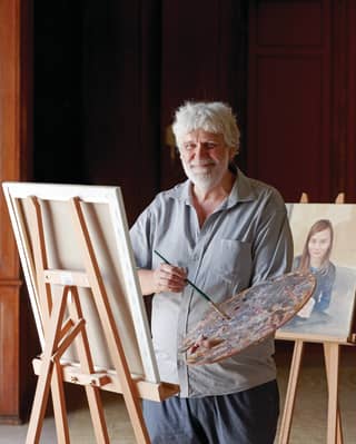 Artist Cyril Coetzee holding a paint palette and smiling at the camera