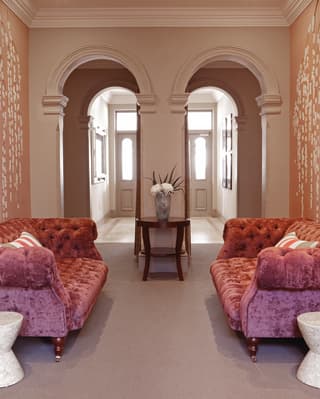 Two pink velvet sofas in a spa waiting room with pink floral wallpaper