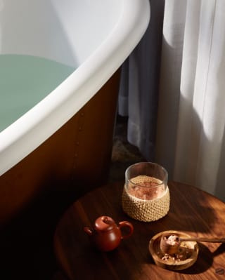 Snapshot of a table with a drink, pot and petals next to a white enamel and cast-iron bath at Librisa Spa.