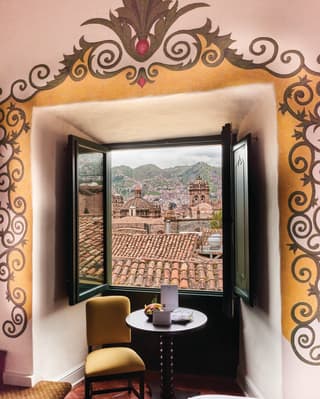 Open window in a yellow hotel room with views across the clay tiled-roofs of Cusco