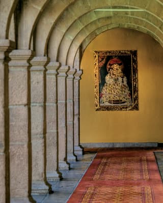 An old religious painting hangs in a hotel corridor between stone pillars and ceiling arches