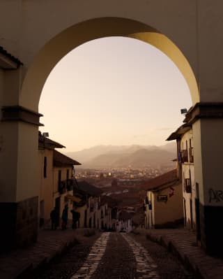 An old cobble road leads under an archway heading towards distant hazy mountains beyond the city