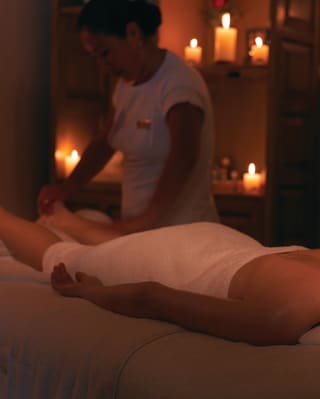 Spa therapist massaging the legs of a guest in a candlelit spa room