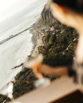 An Observatory guest holds a cocktail in soft-focus, illuminated by sun, as they look out over the dramatic Lima coastline.