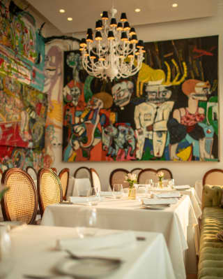 Tables at Tragaluz are embraced by the eclectic flamboyancy of bright wall art by local artists beneath a  Cortez chandelier.