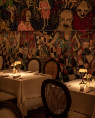 A large characterful mural by Mateo Liébana watches over two dining tables with small glowing lamps at Tragaluz.