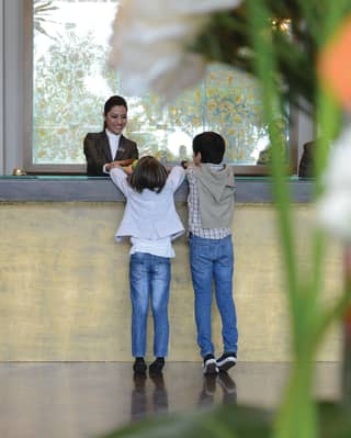 Two kids talking to a concierge at a grey and gold desk with flower arrangements