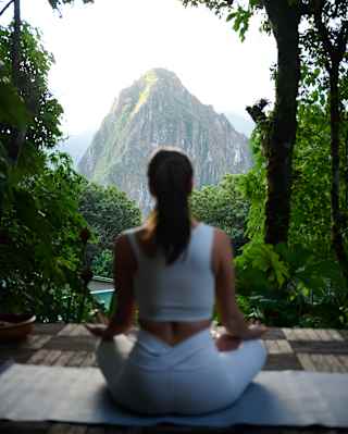 A guest sits in easy pose as she does yoga at the relaxation area, with incredible views of Machu Picchu, seen from behind.