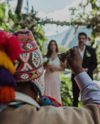 A shaman rings a hand bell before a bride and groom during an Andean ceremony to renew wedding vows, seen from behind.