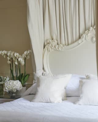 View through four-poster curtains of an ornate white-framed pillowy bed