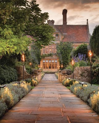 Stone-paved candlelit path leading to a rural manor house in evening light
