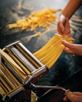 Hands pulling strips of freshly made linguine pasta from a pasta maker