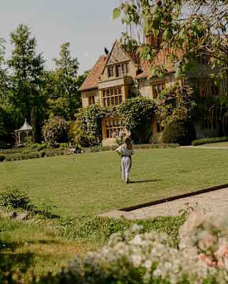 A florist walks across a well-kept sunny lawn on her way to Le Manoir, seen from the gardens.