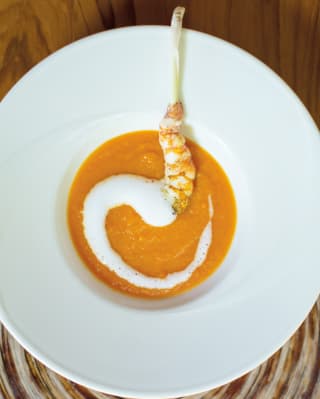 Skewered prawn atop two purees on a round white plate