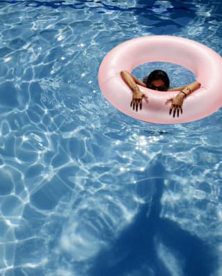 Mulher em uma piscina olhando sobre a borda de uma boia inflável rosa