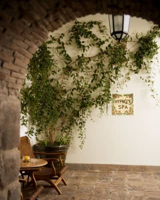 A Hypnôze Spa sign against the wall, near a leafy pot, two chairs and a table