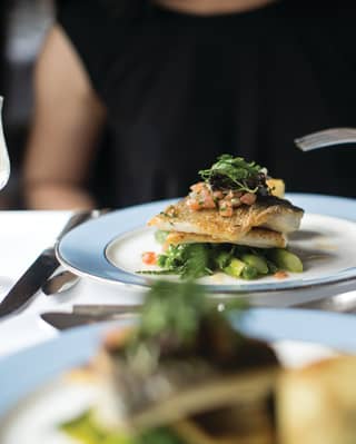 A fish course is an artful tower of crispy skinned white fillet , stacked on a base of asparagus and peas and topped with salsa