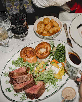Diners enjoy roast beef, presented in slices with Yorkshire puddings, carrots, beans, potatoes and gravy, seen from above.
